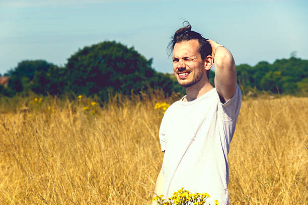 Man Standing in Field of Dry Grass Young man enjoying sunshine with squinty eyes in field of golden grass for concept use squint eyes stock pictures, royalty-free photos & images
