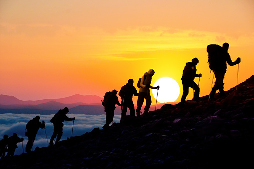 Silhouettes of hikers climbing the mountain at sunset.
