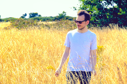 Young man enjoying sunshine with sunglasses in field of golden grass for concept use