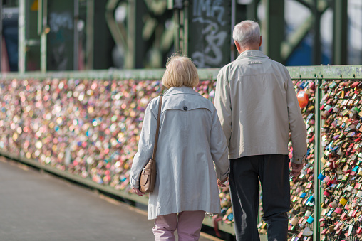 Cologne, Germany - September 22, 2016: real love - Senior couple hand in hand at the bridge of love padlocks. This bridge - the Hohenzollern bridge in Cologne Germany is full of love padlocks. A lot of young couples have made this padlocks over the years, so its a sightseeing of Cologne to walk over this bridge and read the messages. 