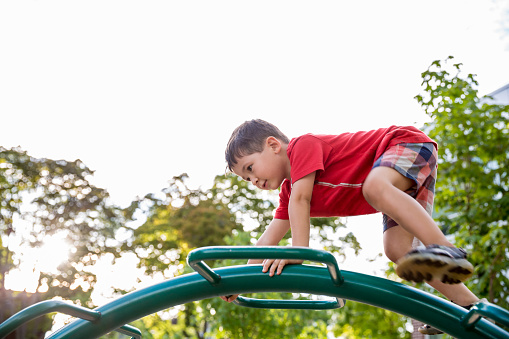 Little boy high up on a playground play structure climbing and balancing while succeeding on getting to the top