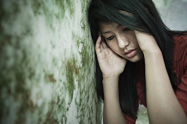Sad girl thinking, looking down while leaning against dirty wall.