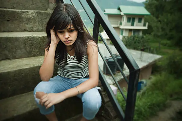 Photo of Sad Asian girl sitting on steps in hilly area.