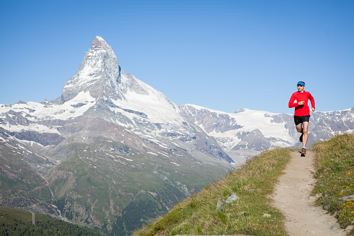 Running high up in the Swiss Alps a male runs next to a lake with the Matterhorn in the background