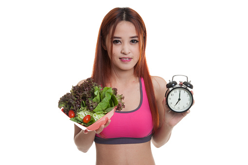 Beautiful Asian healthy girl with clock and salad  isolated on white background.