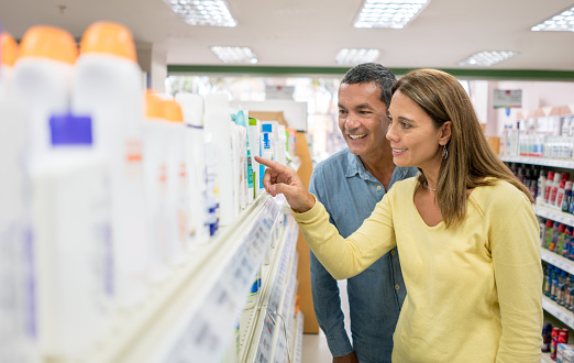 Happy couple of customers shopping at a pharmacy and pointing at some products