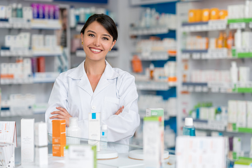 Happy female pharmacist working at a drugstore and looking at the camera smiling