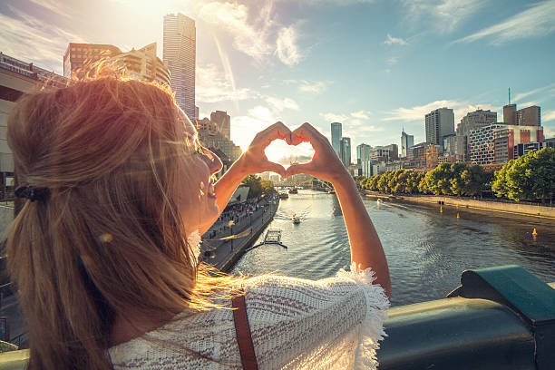 Young woman loving Melbourne, Australia Cheerful young woman in Melbourne makes a heart shape finger frame. She is standing on a bridge overlooking the Melbourne CBD along the Yarra River on a beautiful day. victoria australia photos stock pictures, royalty-free photos & images