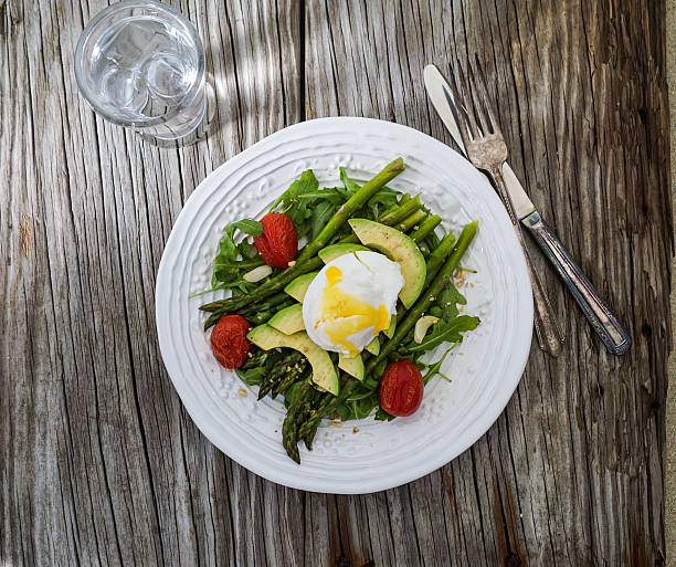 Asparagus with poached egg, avocado and cherry tomatoes seasoned with parmesan on wood background, top view. Healthy lunch concept.