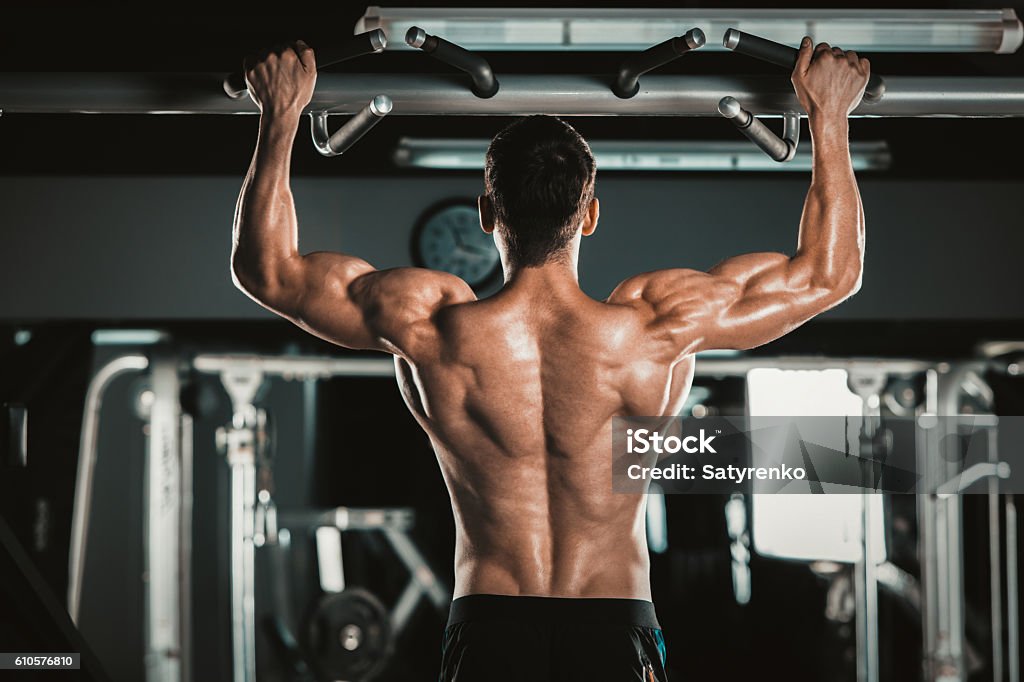 Athlete muscular fitness male model pulling up on horizontal bar Athlete muscular fitness male model pulling up on horizontal bar in a gym. Muscular Build Stock Photo