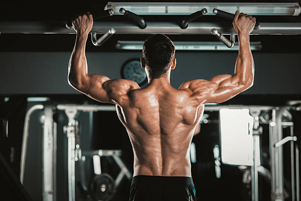 Athlete muscular fitness male model pulling up on horizontal bar Athlete muscular fitness male model pulling up on horizontal bar in a gym. muscular build stock pictures, royalty-free photos & images