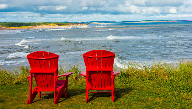 Shoreline plus red chairs  Prince Edward Island National Park The shoreline at Cavendish in Prince Edward Island National Park. The red rocks and sand are natural phenomenonsin the park. September The red Adirondack chairs were placed in all canadian National parks. cavendish beach stock pictures, royalty-free photos & images