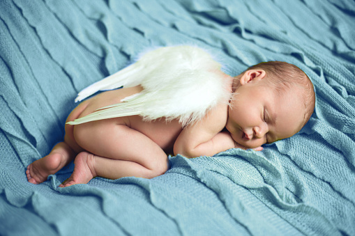 Baby newborn with angel wings lying on the bed and sleeping