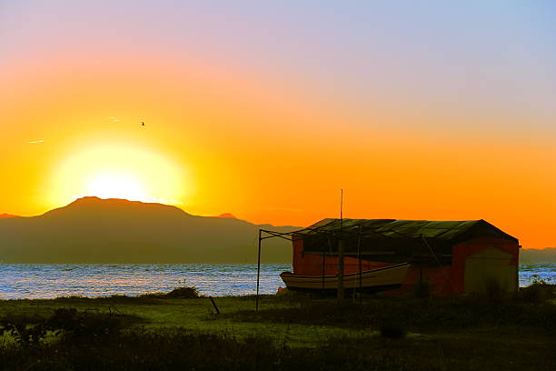 Fisherman's hut at sunset. Fisherman's hut and boat at sunset, on Ponta Das Canas Beach, Florianópolis, southern Brazil. small houseboats stock pictures, royalty-free photos & images
