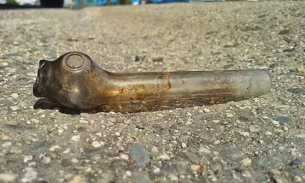 A dirty glass crack pipe lies in the gutter at the side of the road.