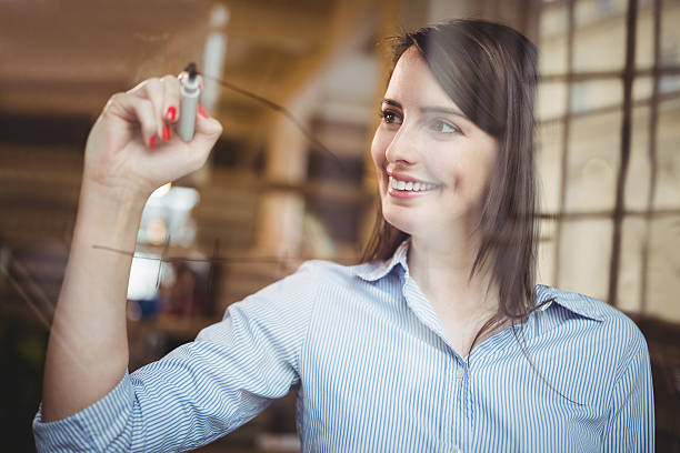 istock Businesswoman smiling while writing on glass with marker pen 610656464