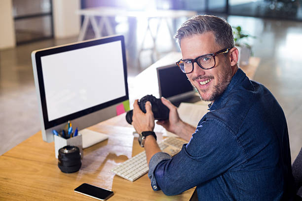 Portrait of smiling man holding camera at table in office
