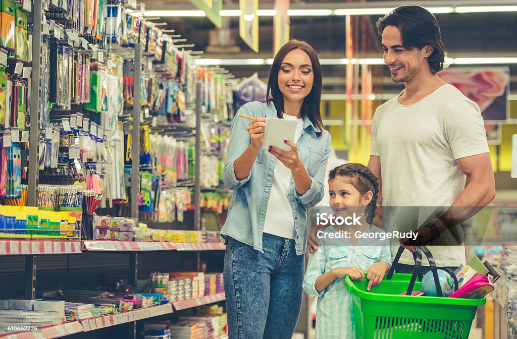 Family in the supermarket Beautiful young parents and their cute little daughter are smiling while choosing school stationery in the supermarket. Mom is making notes in the list Shopping Stock Photo