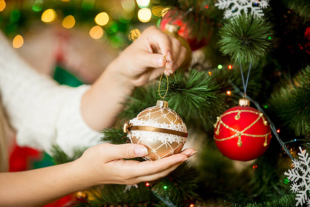 gros plan d’une femme en pull décorant un arbre de noël avec des boules - christmas christmas ornament human hand decoration photos et images de collection