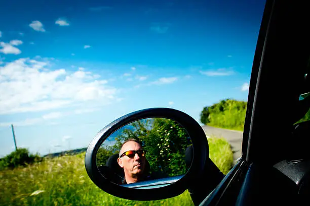 A BMW Mini Cooper S convertible door mirror and background of the beautiful Cambridgeshire countryside. Mature male in sunglasses is visible in the door mirror.