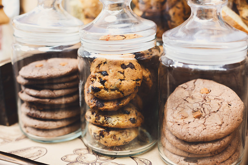 Desserts choice. Cookies and biscuits in glass jars on counter bar for sale. Chocolate drops and chips, oatmeal cookies stacks.