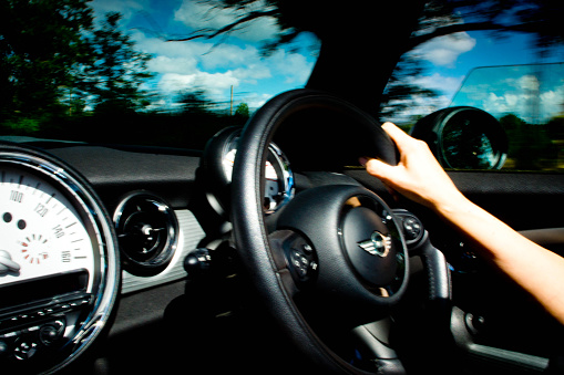 Cambridge, UK - June 27, 2015: A BMW Mini Cooper S convertible interior with the steering wheel prominent in the image. The image was taken whilst the car was moving with a slow shutter speed therefore there is motion blur.