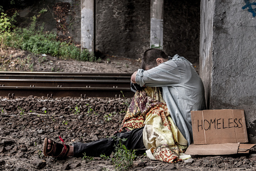 Poor homeless woman with sign sitting on the street near the rail track