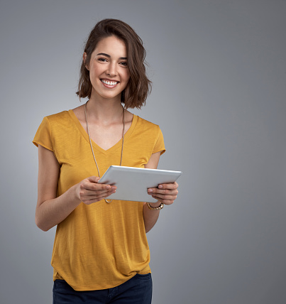 Portrait of an attractive young woman using a digital tablet against a gray background