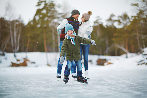 Happy boy on skates looking at camera with his parents behind