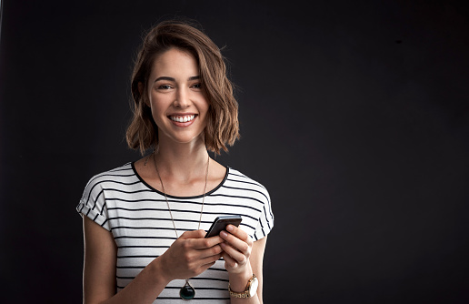 Studio portrait of an attractive young woman using her phone against a black background