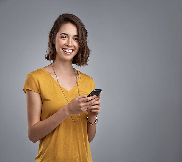 I'm a real fan of my new smartphone Studio portrait of an attractive young woman using her phone against a gray background one young woman only stock pictures, royalty-free photos & images