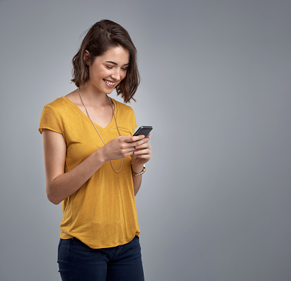 Studio shot of an attractive young woman using her phone against a gray background