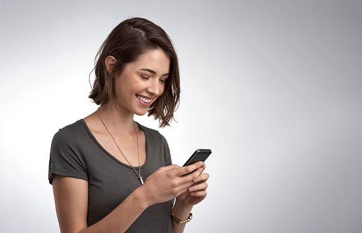 Studio shot of an attractive young woman using her phone against a gray background