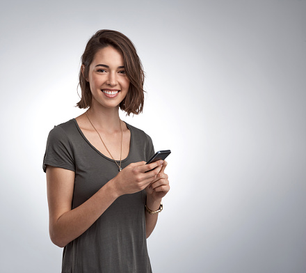 Studio portrait of an attractive young woman using her phone against a gray background