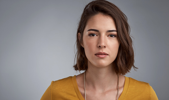 Studio portrait of a young woman looking serious against a gray background