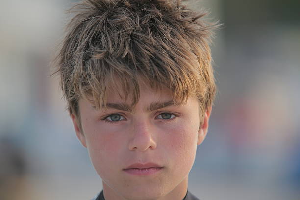 A 13-year-old boy with damp, tousled hair looks downward, absorbed in thought. The room enjoys warm lighting that enhances the thoughtful atmosphere.