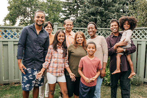 beautiful family with two girls is standing in meadow near walnut tree and has light outfit on and jeans and is happy