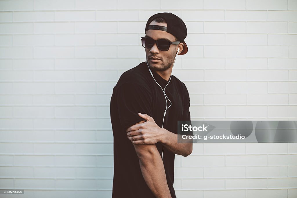 Cool and handsome. Handsome young African man in headphones looking over shoulder while standing in front of the stoned wall outdoors Men Stock Photo