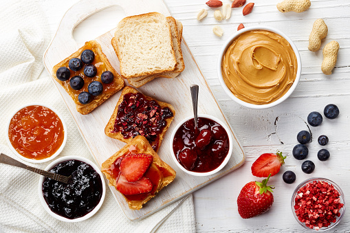 Sandwiches with peanut butter, jam and fresh fruits on white wooden background from top view
