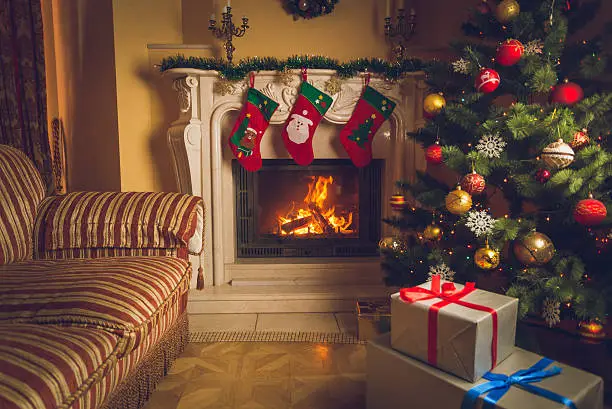 Toned interior image of living room with burning fireplace, decorated Christmas tree and stack of gifts