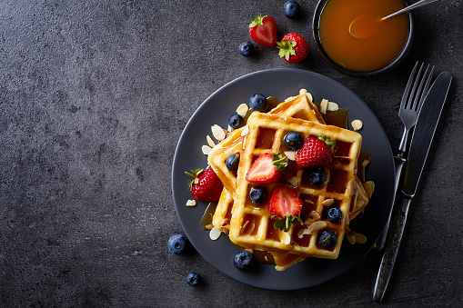 Plate of belgian waffles with caramel sauce and strawberries on dark gray background. From top view