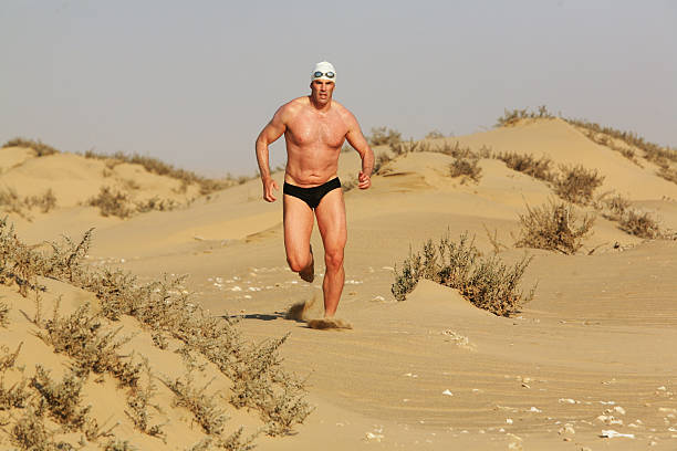 homem corre ao longo da duna com plantas de matagal - calções de corrida - fotografias e filmes do acervo
