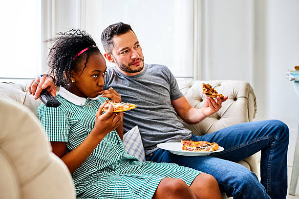 istock Father and daughter eating pizza and watching TV 610750078