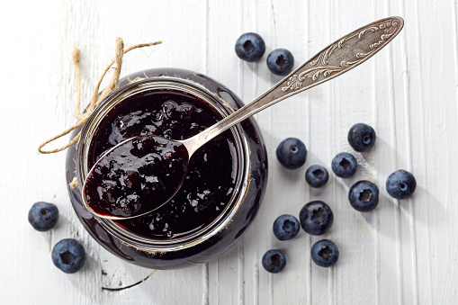 Jar of blueberry jam on white wooden background from top view