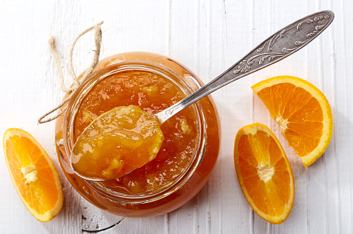 Jar of orange jam on white wooden background from top view