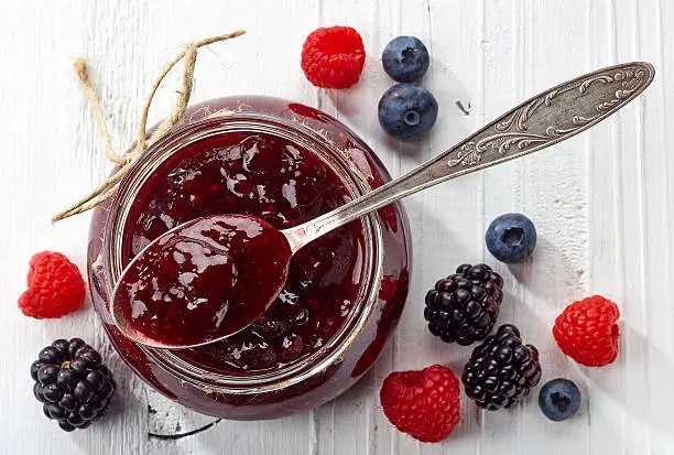 Jar of wild berry jam on white wooden background from top view