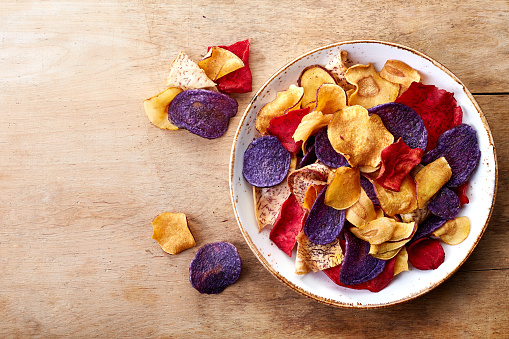 Bowl of healthy colorful vegetable chips on wooden background from top view