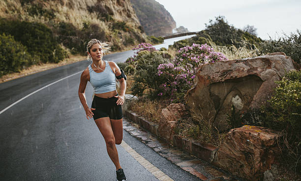 Woman running on the road around mountains Fitness woman running on the road around mountains under rain. Female athlete training outdoors. hard and fast stock pictures, royalty-free photos & images