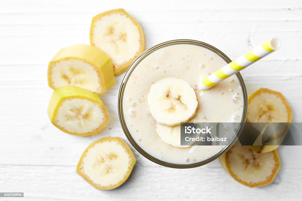Glass of banana smoothie Glass of banana smoothie on white wooden background from top view Banana Stock Photo
