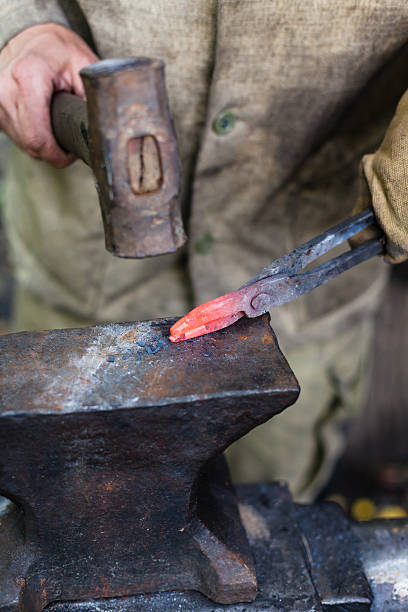 istock Blacksmith forges tongs with hammer on anvil 610757638